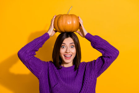 Portrait of excited cheerful person arms hold pumpkin head toothy smile isolated on yellow color backgroundの写真素材