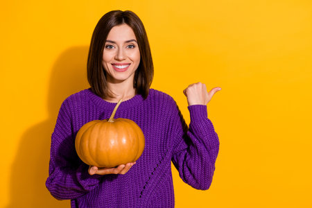 Portrait of pretty positive lady hold pumpkin direct thumb finger empty space isolated on yellow color backgroundの写真素材