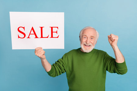Photo of delighted satisfied funny granddad raise fist celebrate luck success isolated on blue color backgroundの写真素材