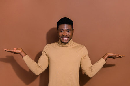 Photo of funny young brunet guy hold empty space wear beige shirt isolated on brown color backgroundの写真素材