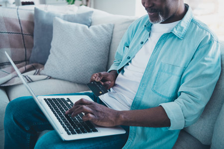 Cropped photo of aged man client offer gifts online use deposit card profit netbook in modern living roomの写真素材