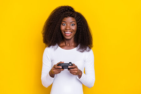 Photo of excited positive girl hold controller playing games isolated on yellow color backgroundの写真素材