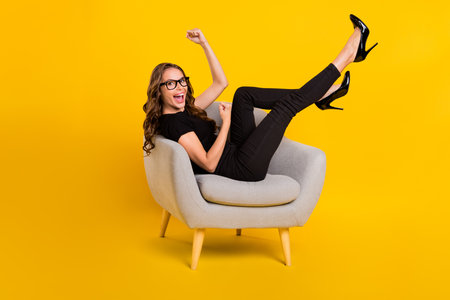 Full body profile side photo of young excited lady sitting chair celebrate success fists hands isolated over yellow color backgroundの写真素材