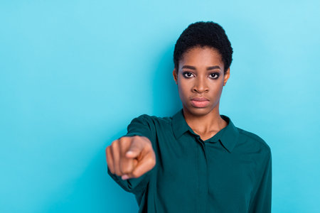 Photo of serious strict androgynous human wear green shirt pointing finger you empty space isolated blue color backgroundの写真素材