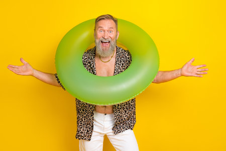 Photo portrait of attractive grandpa hold inflatable buoy neck wear trendy leopard print outfit isolated on yellow color backgroundの写真素材