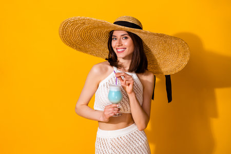 Photo of pretty stunning lady wear white outfit hat smiling enjoying blue cocktail isolated yellow...