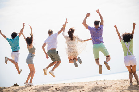 Full size rear behind portrait of company crazy ecstatic fellows jumping raise fists sunny weather water sand beach outdoorsの写真素材
