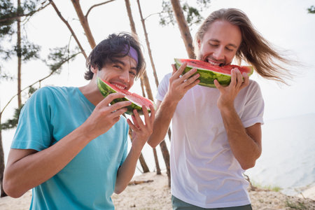 Photo of enjoy guys eat watermelon wear casual cloth outdoors on the river near treesの写真素材