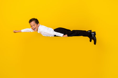 Full length profile photo of energetic cheerful boy flying empty space isolated on yellow color backgroundの写真素材