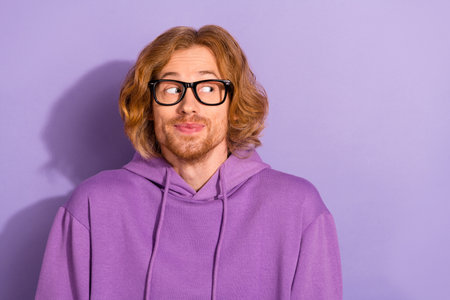 Photo of shy wavy orange hairdo guy look promo wear eyewear violet hoodie isolated on purple color backgroundの写真素材