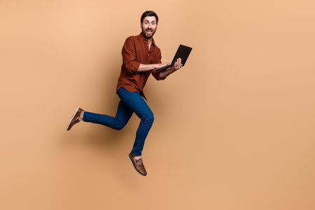 Full length profile portrait of energetic excited guy hold use netbook jump run empty space isolated...
