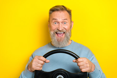 Photo of charming excited man pensioner dressed blue pullover open mouth riding auto isolated yellow color backgroundの写真素材