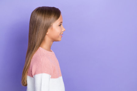 Profile side photo of attractive little lady look empty space dressed colorful pullover toothy smile isolated on purple color backgroundの写真素材