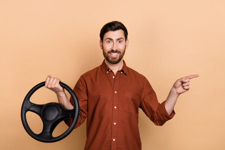 Portrait of cheerful positive guy hold wheel indicate finger empty space offer isolated on beige color backgroundの写真素材