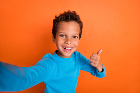 Photo portrait of adorable little boy video call show thumb up good job feedback wear trendy blue look isolated on orange color backgroundの写真素材