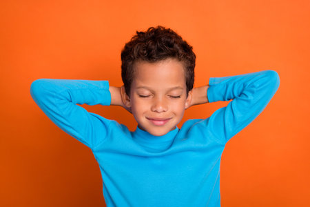 Photo of cute sleepy attractive boy arm behind head free time relax wear blue stylish pullover isolated on orange color backgroundの写真素材