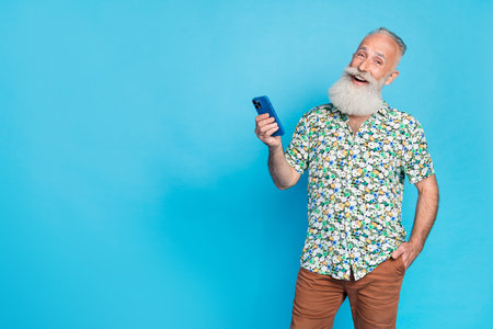 Photo of handsome positive man hold telephone empty space ad isolated on blue color backgroundの写真素材