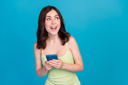 Photo of shiny excited girl dressed green clothes writing modern device looking empty space isolated blue color backgroundの写真素材