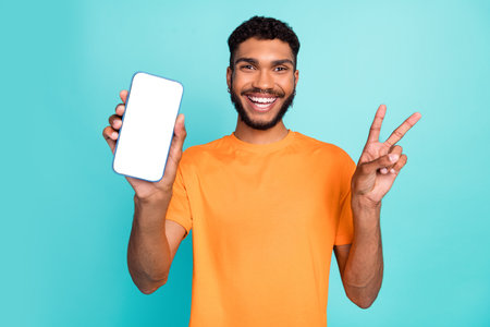Portrait of handsome positive guy demonstrate empty space telephone v-sign isolated on teal color...