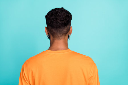 Photo of attractive handsome man dressed orange t-shirt standing back showing new haircut isolated turquoise color backgroundの写真素材