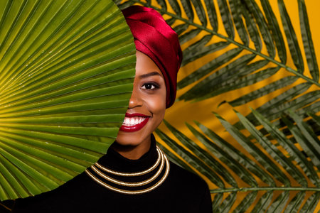 Portrait of positive cheerful lady green leaves cover eye kenya national headwear isolated on yellow...