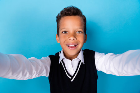 Photo of positive charming little guy dressed black vest smiling recording self video isolated blue...