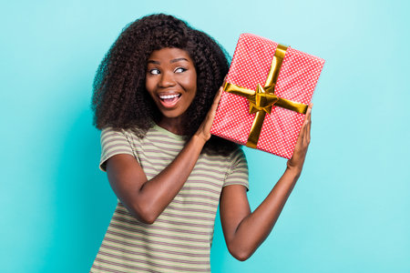 Photo of dreamy excited lady wear striped t-shirt guessing what inside gift box isolated turquoise color backgroundの写真素材