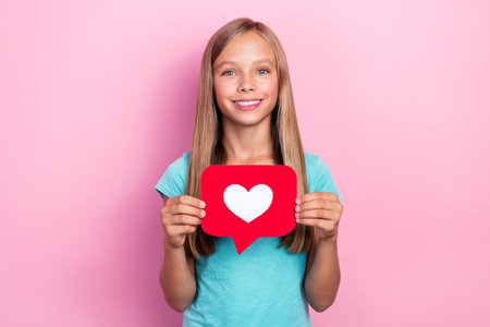 Photo of good mood pretty little child dressed teal t-shirt holding heart like postcard isolated...