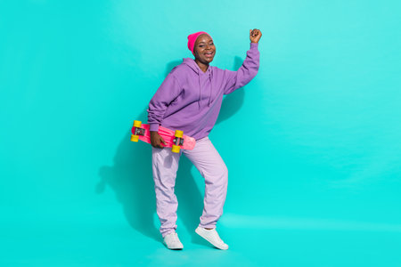 Full length body size view of attractive girl holding skate dancing celebrating isolated over bright teal turquoise color backgroundの写真素材