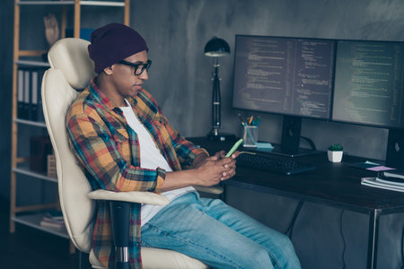 Photo of cool happy guy dressed eyewear hat chatting modern device indoors workstation workshop homeの写真素材
