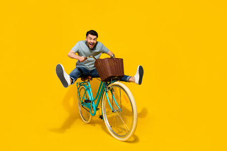 Full length photo of young funky energetic guy riding retro eco bicycle with busket legs up crazy excited isolated on bright yellow color backgroundの写真素材