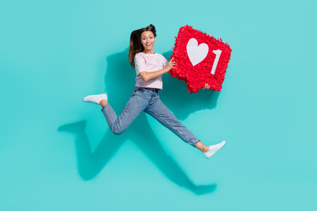Photo of excited impressed woman with straight hairstyle wear striped t-shirt running hold big like isolated on teal color backgroundの写真素材