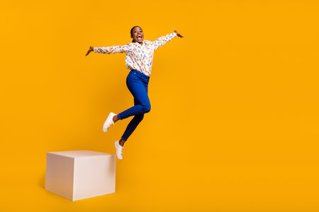 Full length body size view of attractive cheery girl jumping from stage having fun isolated over bright yellow color backgroundの写真素材