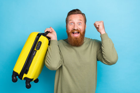Photo portrait of nice young guy excited raise fist suitcase travel agency discount wear khaki...