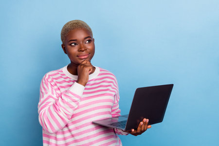 Portrait of young minded girl hold hand laptop touching chin looking empty space isolated on blue...