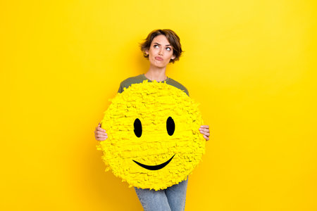 Photo of minded lady hold big paper card poster interested look empty space consider dilemma decision isolated on yellow color backgroundの写真素材