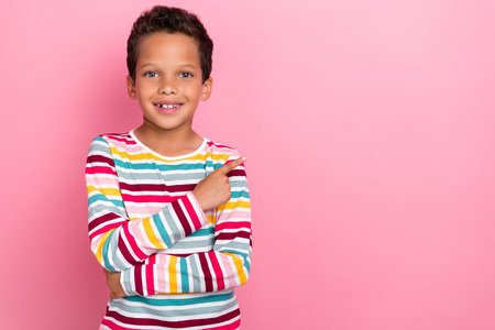 Portrait of adorable schoolboy with curly hairstyle dressed striped long sleeve indicating empty...