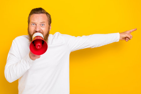 Photo portrait of handsome young man strict boss shout yell order megaphone wear stylish white garment isolated on yellow color backgroundの写真素材