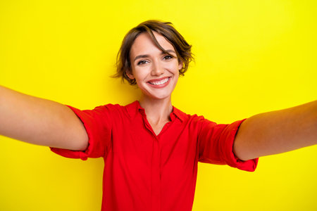 Photo of nice sweet pretty positive cheerful girl with bob hairstyle dressed red shirt doing selfie isolated on yellow color backgroundの写真素材