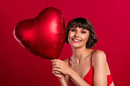 Portrait of attractive cheerful gorgeous girl holding helium ball heart shape 14 February party isolated on bright red color backgroundの写真素材