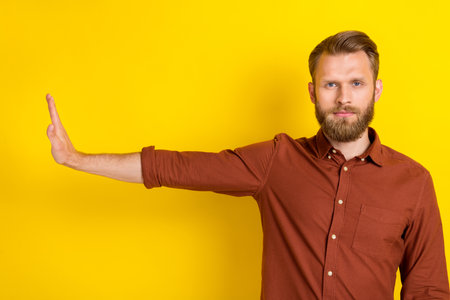 Portrait of focused concentrated person arm palm block empty space isolated on yellow color backgroundの写真素材