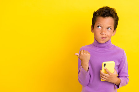 Photo of small schoolboy hold telephone look indicate thumb finger empty space isolated on yellow color backgroundの写真素材