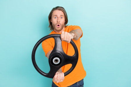 Photo of young bearded handsome funny man wear orange t-shirt driving steering wheel shocked car...