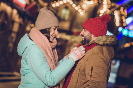 Profile portrait of attractive lady fixing handsome guy scarf advert garland lights evening outsideの写真素材