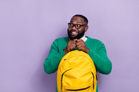 Portrait of cheerful minded man hold backpack look interested empty space isolated on purple color...