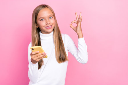 Photo of pretty little girl schoolgirl stylish outfit hand okey symbol rejoice modern gadget empty space isolated on pink color backgroundの写真素材