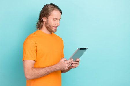 Photo of positive cute guy dressed orange t-shirt chatting apple modern gadget empty space isolated teal color backgroundの写真素材