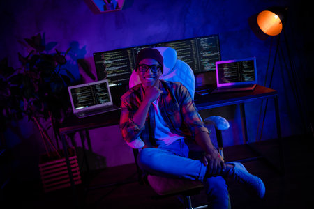 Photo of positive intelligent hacker sitting chair hand touch chin server operating evening loft room indoorsの写真素材