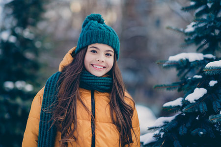 Photo of pretty cheerful school girl dressed outwear coat smiling walking snowy pine countryside forestの写真素材