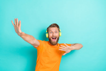 Photo of impressed beard guy listen music dance wear headphones orange t-shirt isolated on turquoise color backgroiundの写真素材